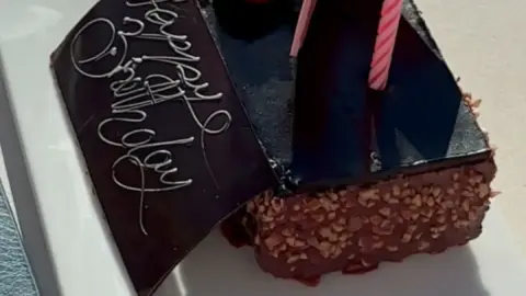Slim brunette blows out candle on birthday cake in cafe