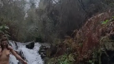 Nude brunette with face paint soaping up in waterfall scene