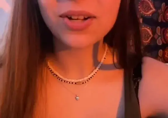 Brunette girl teases camera with heart necklace in dim room