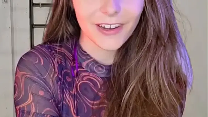 Brunette in purple lighting smiles while sitting on chair in studio