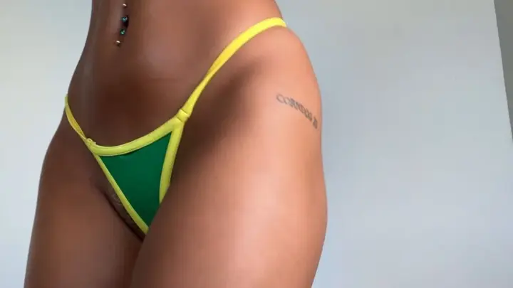 Tan brunette in green-yellow bikini poses nude, tattoos, navel pierce