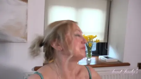 Blonde MILF in lingerie laughs before stripping topless on bed