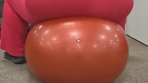 Curvy brunette bouncing on exercise ball in gym, tattoo visible