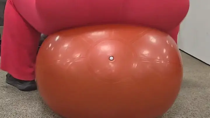Curvy brunette bouncing on exercise ball in gym, tattoo visible